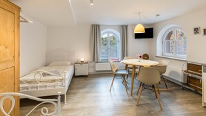A bedroom with a bed, bedside table, lamp, and a window with curtains. - Appartment Kutscherstube (Altensteig)