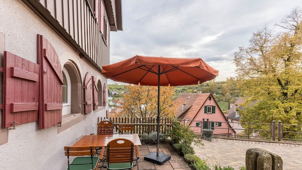 A patio with a table and chairs, an umbrella, and a view of houses in the background. - Appartment Kutscherstube (Altensteig)