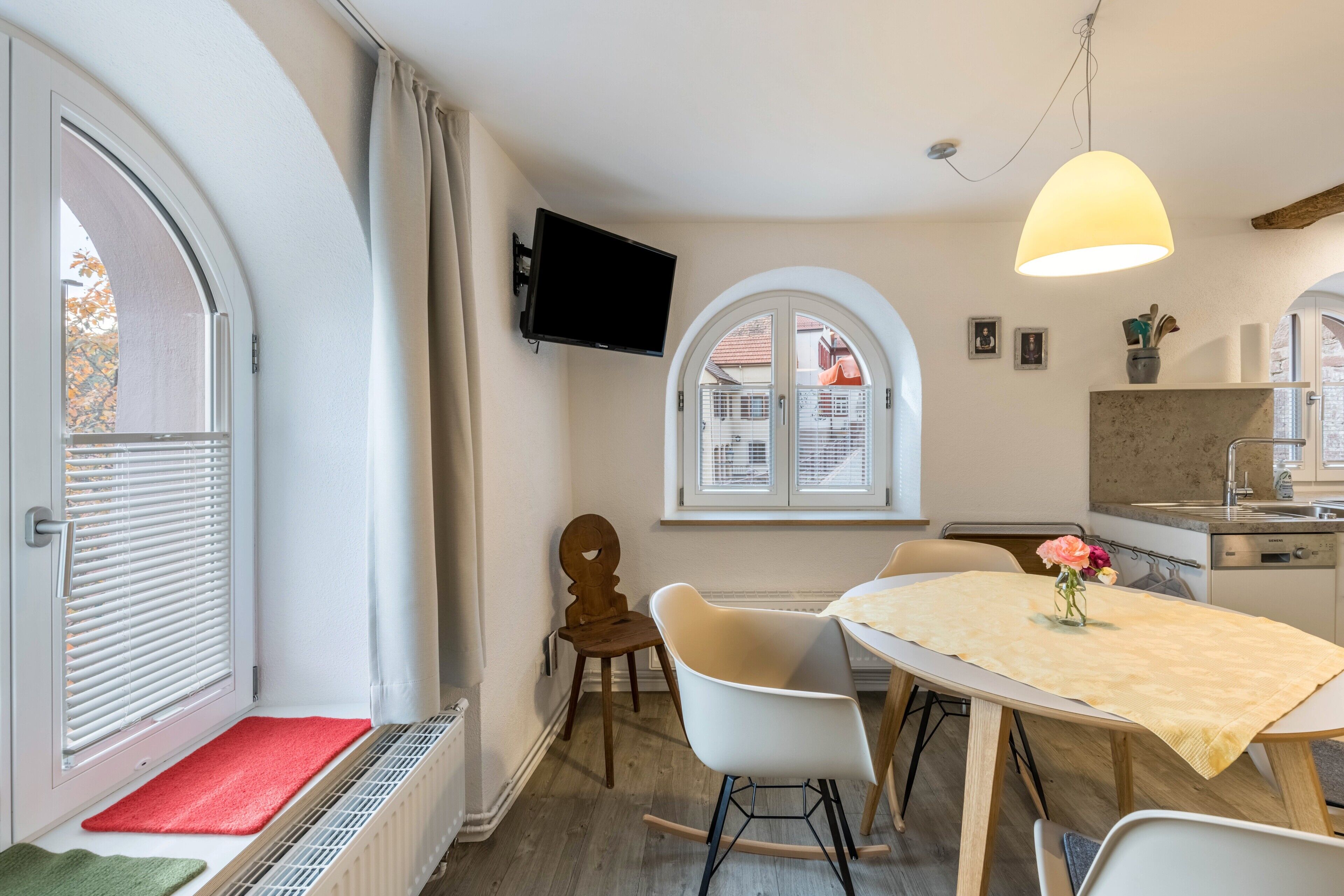Una cucina moderna con zona pranzo, televisore a parete e finestra con persiane.