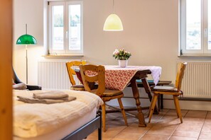 A room with a bed, a dining table with chairs, a potted plant, and a hanging light fixture. - Appartment Krämerstube (Altensteig)