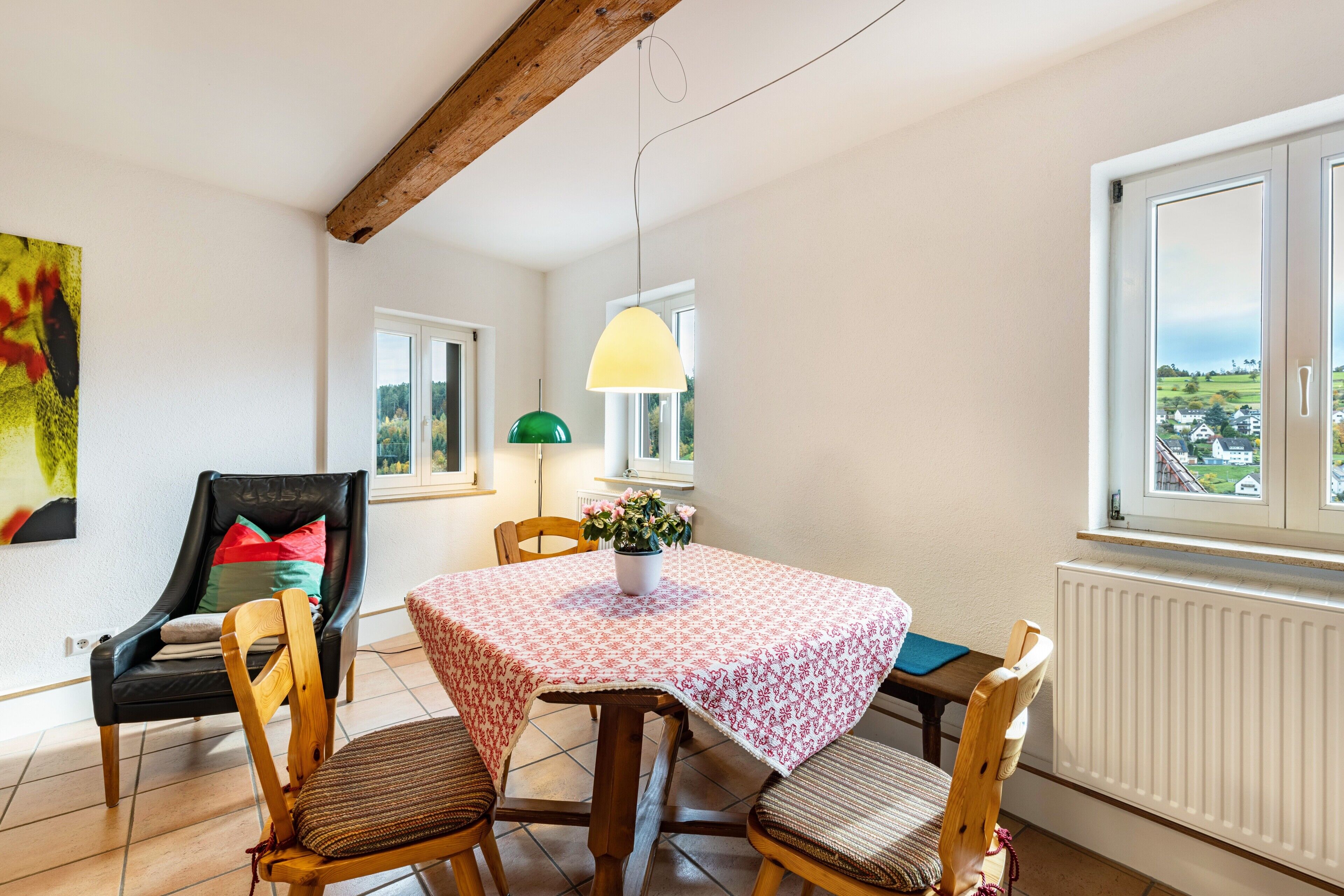 A dining area with a table, chairs, a pendant light, and a view through a window.