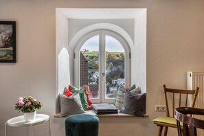 A room with a large arched window, a small table with a potted plant, a cushioned bench, and a wooden chair. - Appartment Storchennest (Altensteig)