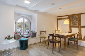 A dining area with a wooden table, chairs, a window with a view, and a small round table with a plant. - Appartment Storchennest (Altensteig)
