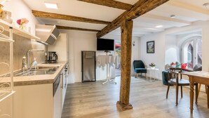 Une cuisine moderne avec des poutres en bois, un coin repas avec une table et des chaises, et un téléviseur fixé au mur.