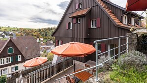 A multi-story building with a balcony, outdoor seating, and a view of a town. - Appartment Apothekerstube (Altensteig)