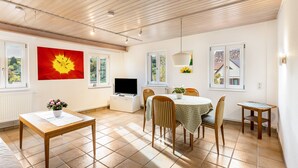 A dining area with a table, chairs, a television, and a window with a view. - Appartment Apothekerstube (Altensteig)