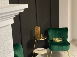 A room with a dark wall, a green chair, a small round table with a gold base, and a white shelf. - Apartment Fewo Lago di Costanza 2 with Private Garden, Lounge & Balcony (Friedrichshafen)