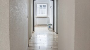 Un pasillo con un radiador, una ventana con persianas y una pequeña mesa con una silla.