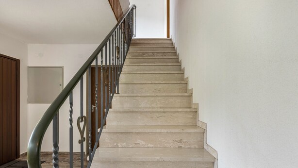 Una escalera con barandilla de metal y peldaños color beige que conduce a una puerta.