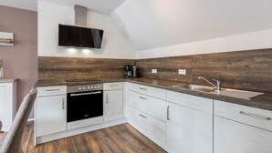 A modern kitchen with a built-in oven, a sink, and a flat-screen TV mounted above the counter. - Apartment 'Ferienwohnung 2, 80qm' with Mountain View, Shared Garden and Wi-Fi (Rosswangen)