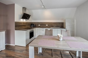 Une cuisine moderne avec des meubles blancs, un plan de travail en bois et un coin repas comprenant une table et des chaises.