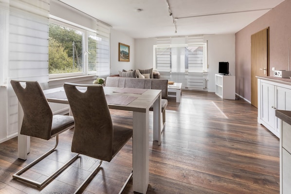 Une cuisine moderne avec un coin repas, un plancher en bois et de grandes fenêtres.