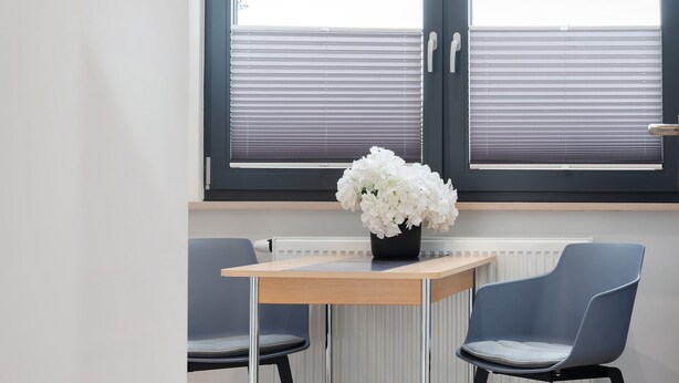 Ein Zimmer mit Tisch, zwei Stühlen, einer Heizung und einem Fenster mit Jalousien.