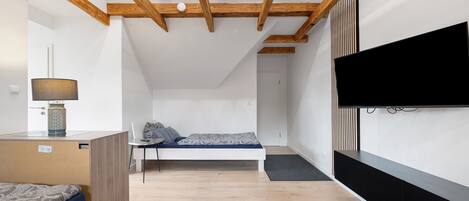 A modern bedroom with a bed, a desk, a lamp, a TV, and a wooden ceiling structure.