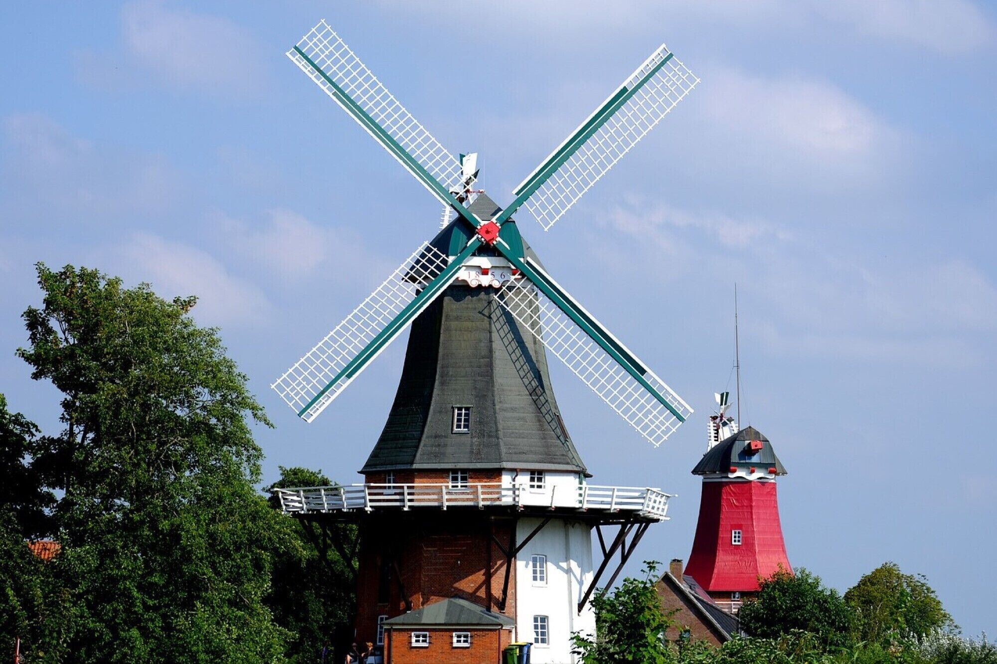 A windmill with a white and red structure, surrounded by trees.
