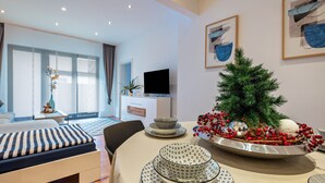 Una habitación de hotel moderna con cama, una mesa de comedor con objetos decorativos, televisión y un árbol de Navidad.