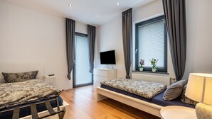 Un dormitorio moderno con cama, mesita de noche, televisor y ventana con cortinas.