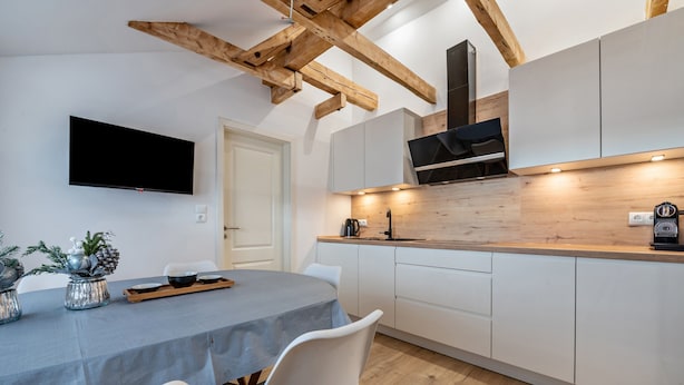 Una cocina moderna con armarios blancos, una encimera de madera y un televisor de pantalla plana montado sobre la encimera.