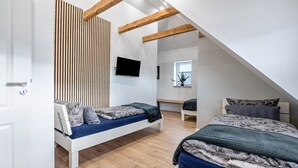 Un dormitorio moderno con dos camas, un televisor, vigas de madera, una ventana y una planta.