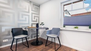 Una habitación con una mesa redonda, dos sillas, una ventana con persianas, un papel tapiz decorado y una planta pequeña en el alféizar.