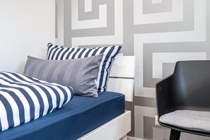 Un lit avec une couette à rayures, un oreiller gris et une chaise noire.