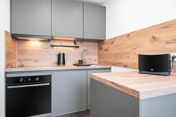 Une cuisine moderne avec des meubles gris, un plan de travail en bois, un four encastré et une machine à café.