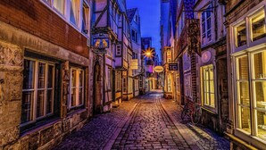 Eine enge Kopfsteinpflasterstraße gesäumt von historischen Gebäuden, mit einem Fahrrad und beleuchteten Schildern.