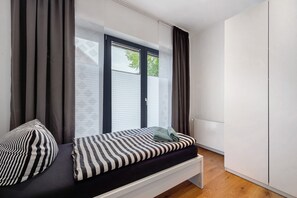 Une chambre à coucher avec un lit, une fenêtre avec des stores, une armoire et un banc.