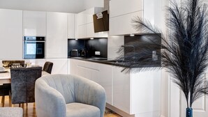 Una cocina moderna con armarios blancos, horno empotrado y un comedor con una silla tapizada en gris.
