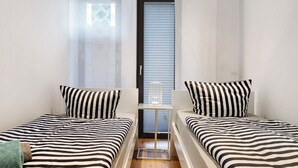 Una habitación con dos camas, una mesita y una ventana con persianas.