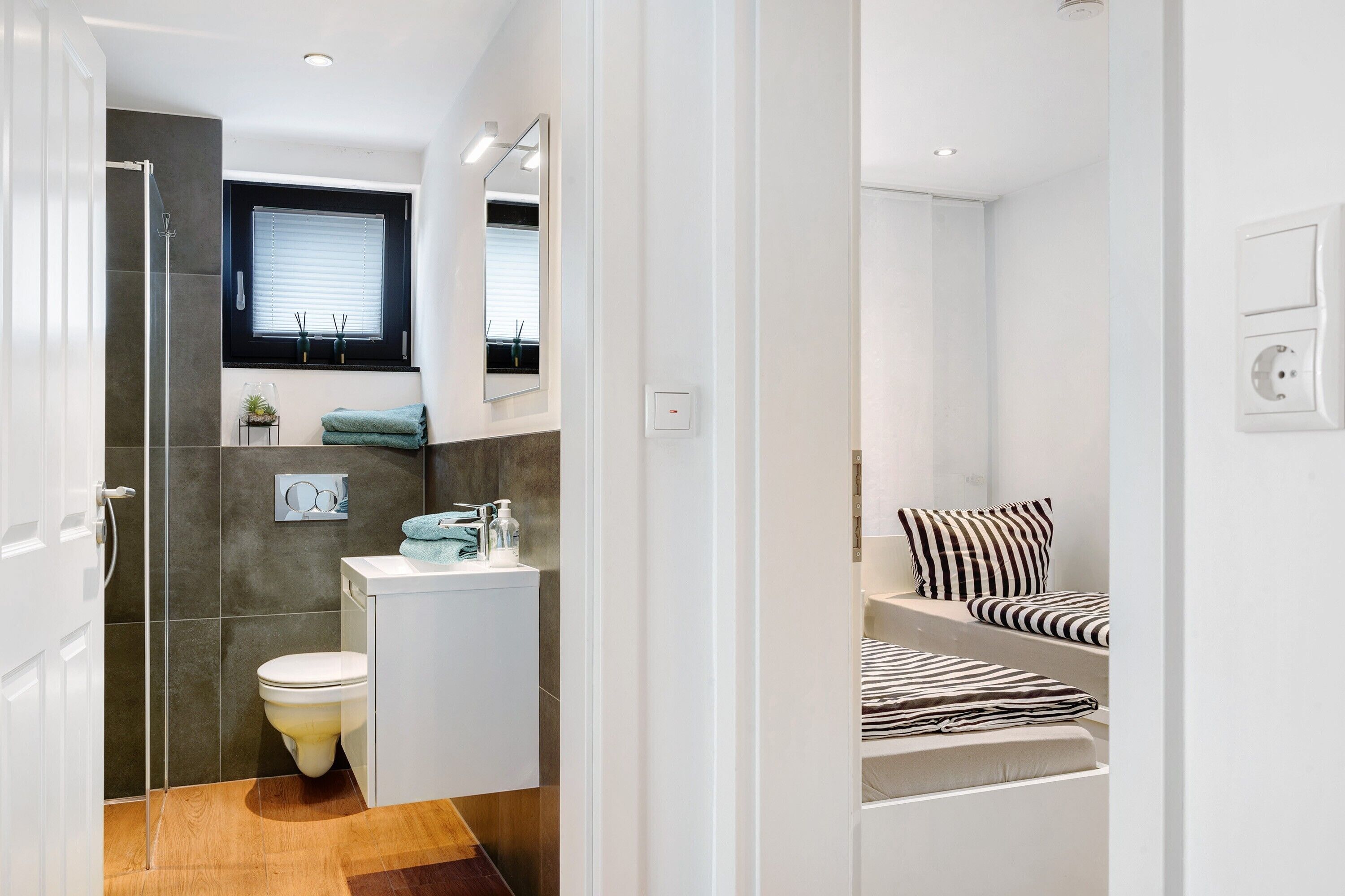 A modern bathroom with a shower, toilet, sink, and a window with blinds.