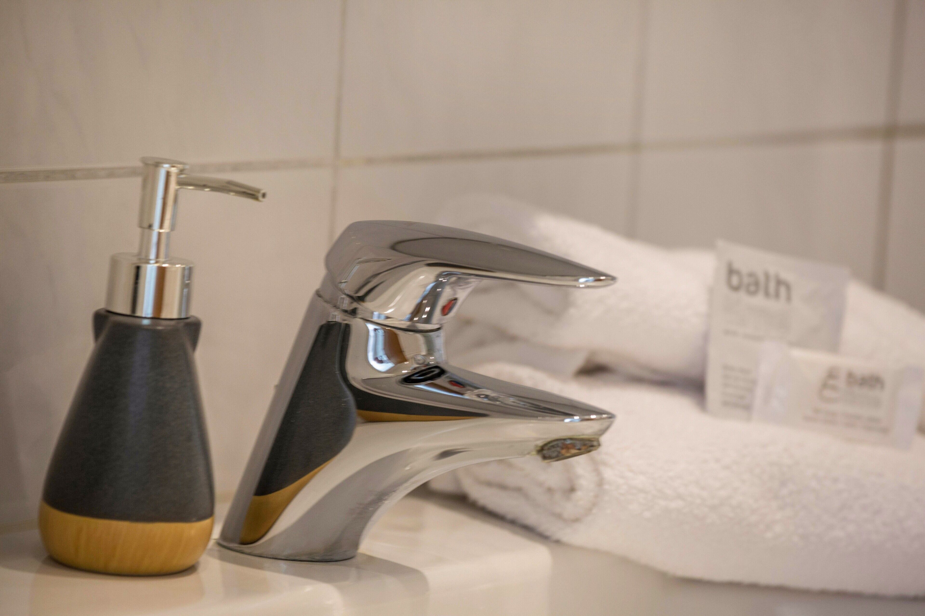 Ein Badezimmer mit einem modernen Wasserhahn, einer Seifenspender und einem Handtuchhalter mit Handtüchern.