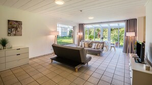 A modern living room with a sofa, a TV, and a dining area with a table and chairs. - Apartment with Conservatory near Movie Park, Private Terrace, and Wi-Fi (Bottrop)