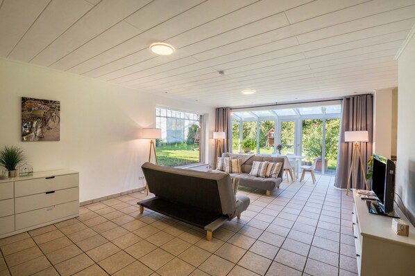 A modern living room with a sofa, a TV, and a dining area with a table and chairs.