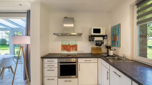 A modern kitchen with a stainless steel range, oven, and microwave, white cabinetry, and a large window providing a view of the outdoors. - Apartment with Conservatory near Movie Park, Private Terrace, and Wi-Fi (Bottrop)