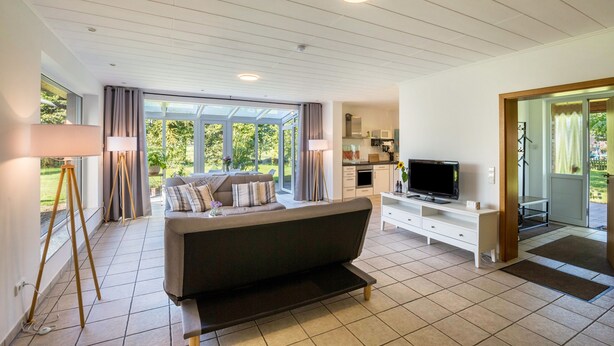 A modern living room with a sofa, TV, and dining area. - Apartment with Conservatory near Movie Park, Private Terrace, and Wi-Fi (Bottrop)