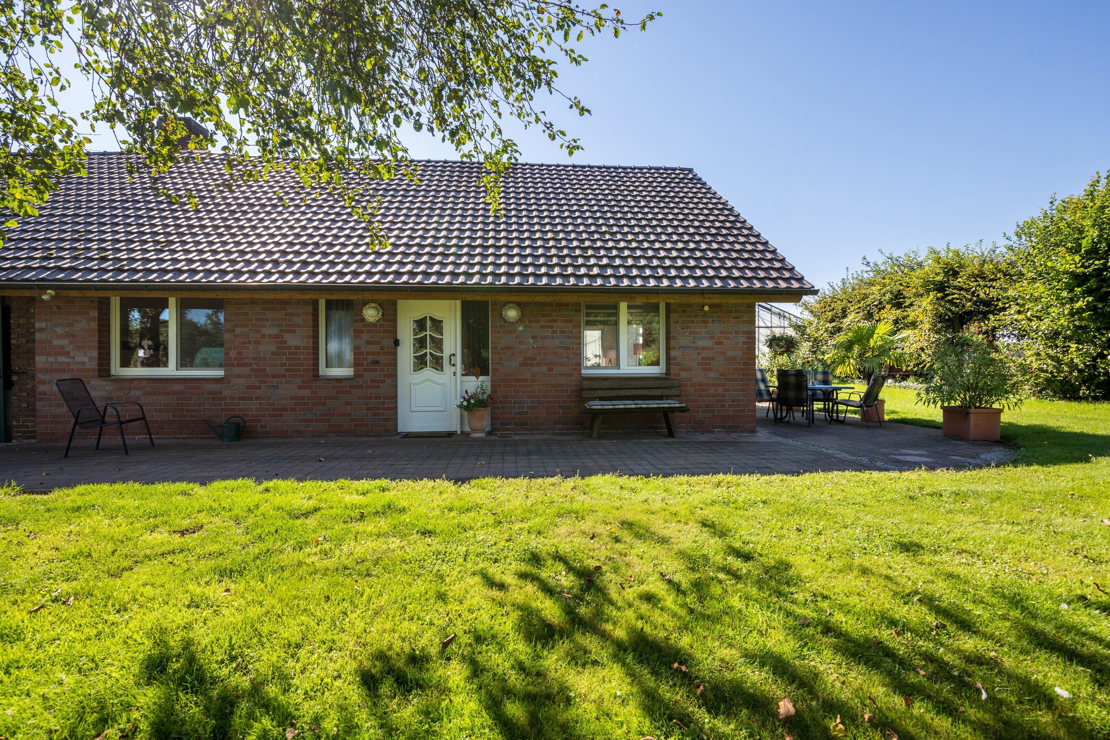 Een bakstenen huis met pannendak, een voordeur en een bankje ervoor.