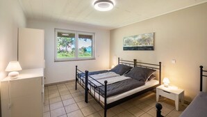A bedroom with a bed, bedside tables, a wardrobe, a window, and a ceiling light. - Apartment with Conservatory near Movie Park, Private Terrace, and Wi-Fi (Bottrop)