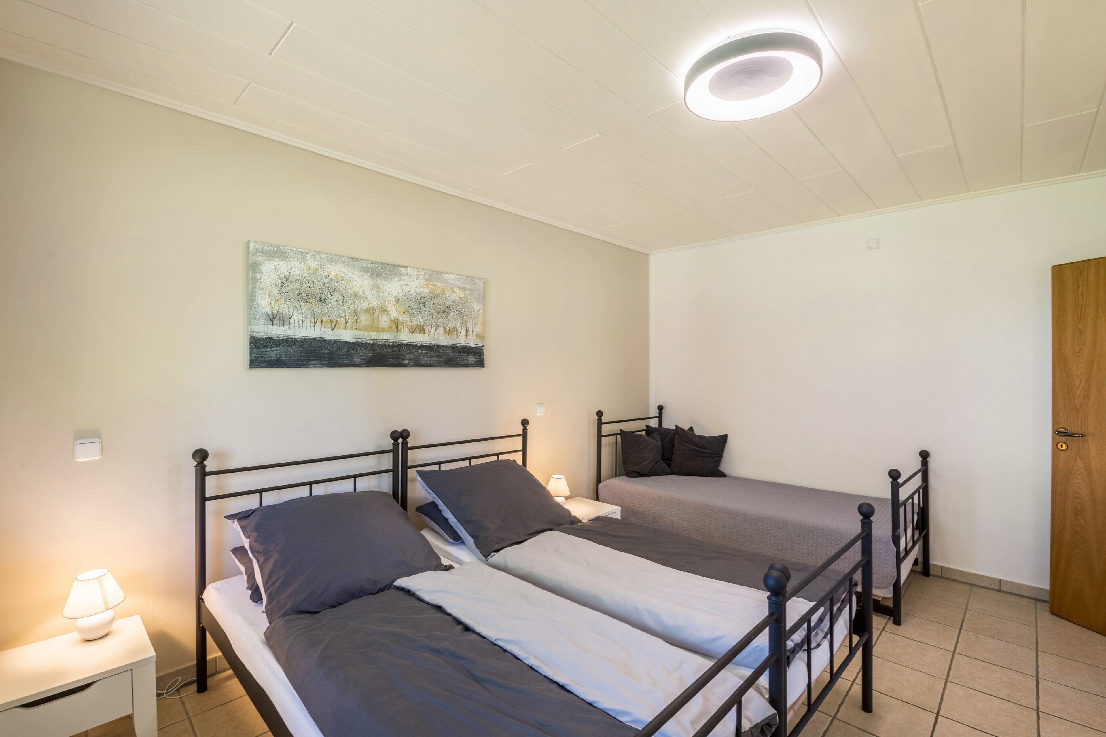 Ein Schlafzimmer mit zwei Betten, einem Nachttisch mit Lampe, einem Bild an der Wand und einer Deckenleuchte.