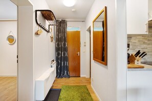 A hallway with a wooden door, a mirror, a kitchen counter with knives, and a green rug.