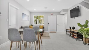 A modern living room with a dining area, a TV mounted on the wall, and a large plant.