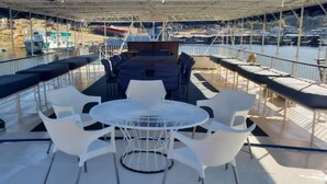 A covered outdoor seating area with a round table and white chairs, overlooking a marina with boats. - Houseboat With Aircon and Splash Pool - 2128 (Kariba)