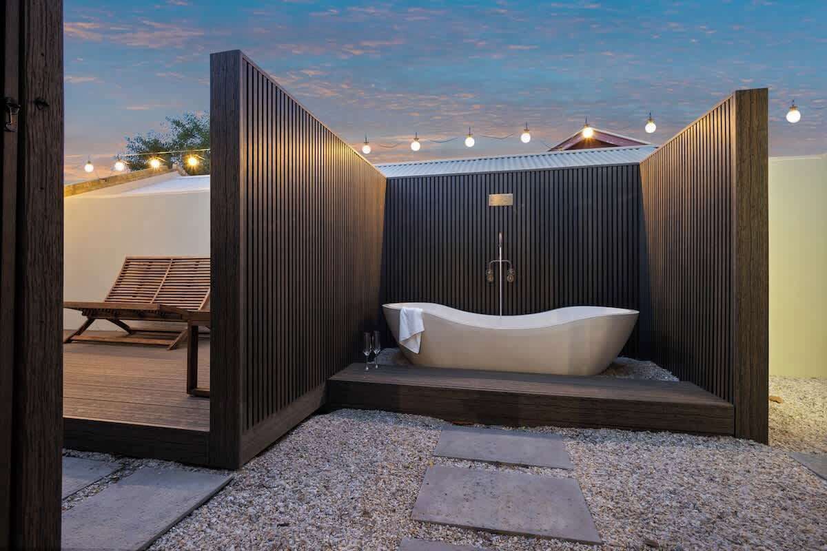 A modern outdoor spa area with a freestanding bathtub, wooden deck, and string lights.