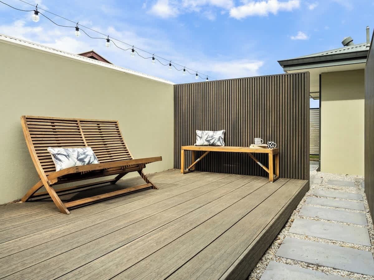 Een houten terras met een lounge stoel en een bijzettafeltje met kussen.