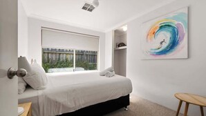 Un dormitorio con una cama, ventana, mesita de noche, una silla y un cuadro abstracto colorido en la pared.