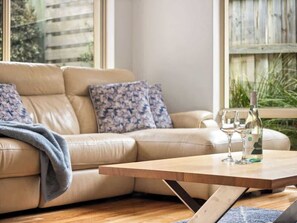 Un salon avec un canapé beige, des coussins à motifs, une table basse en bois et deux verres à vin.