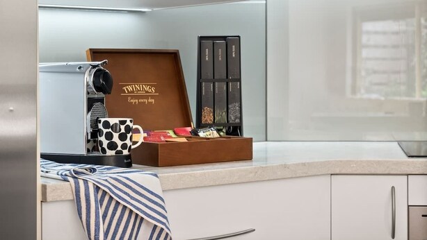 Una cocina con una cafetera, una taza de lunares, una caja de madera con una variedad de granos de café y un armario negro.