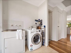 Une buanderie équipée d’un lave-linge, d’un sèche-linge et d’une table à repasser sur laquelle est posée une serviette.