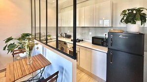 Una cocina moderna con un refrigerador negro, armarios blancos y una mesa de comedor de madera con sillas.
