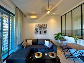 A modern living room with a dark blue sofa, a black coffee table, and a dining area with a wooden table and chairs.